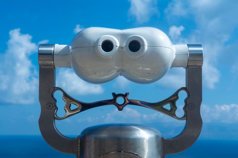 View through coin-operated binoculars with a clear blue sky and ocean horizon.